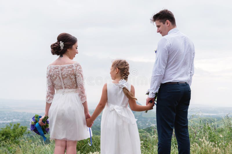 Los jóvenes casados se juntan y su pequeña hija el día de boda se está colocando en la naturaleza que lleva a cabo las manos fotos de archivo libres de regalías