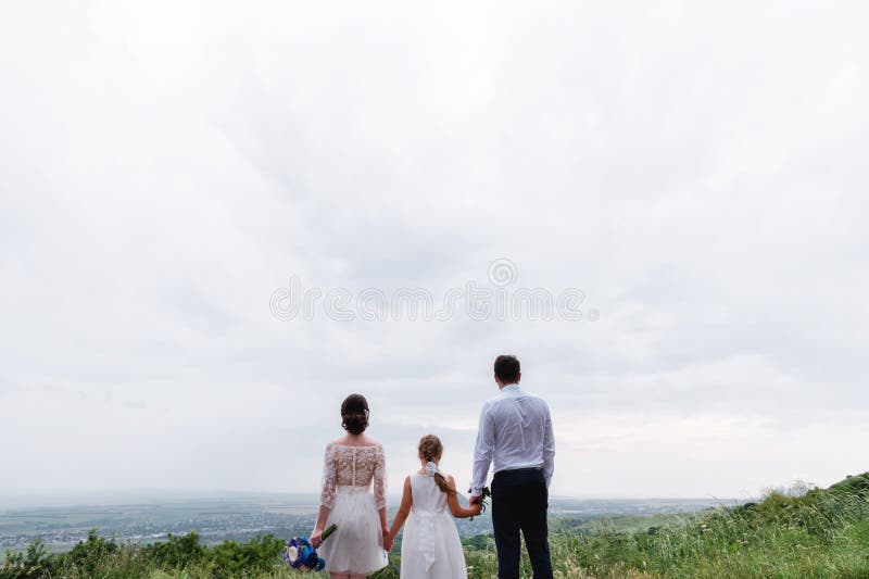Los jóvenes casados se juntan y su pequeña hija el día de boda se está colocando en la naturaleza que lleva a cabo las manos imágenes de archivo libres de regalías