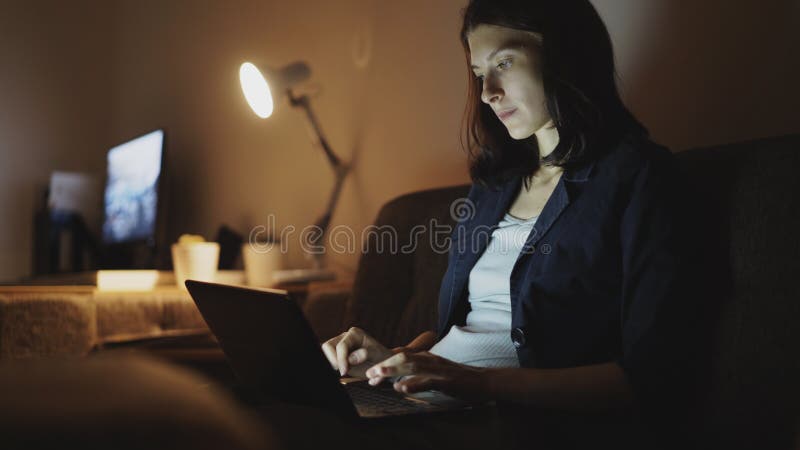 Los jóvenes concentraron a la mujer que trabajaba en la noche usando el ordenador portátil y el mensaje que mecanografiaba fotografía de archivo Los jóvenes concentraron a la mujer que trabajaba en la noche usando el ordenador portátil y el mensaje que mecanografiaba fotografía de archivo