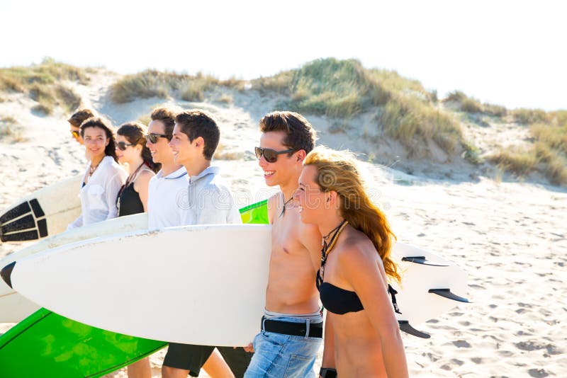 Los muchachos y las muchachas adolescentes de la persona que practica surf agrupan caminar en la playa imagen de archivo Los muchachos y las muchachas adolescentes de la persona que practica surf agrupan caminar en la playa imagen de archivo