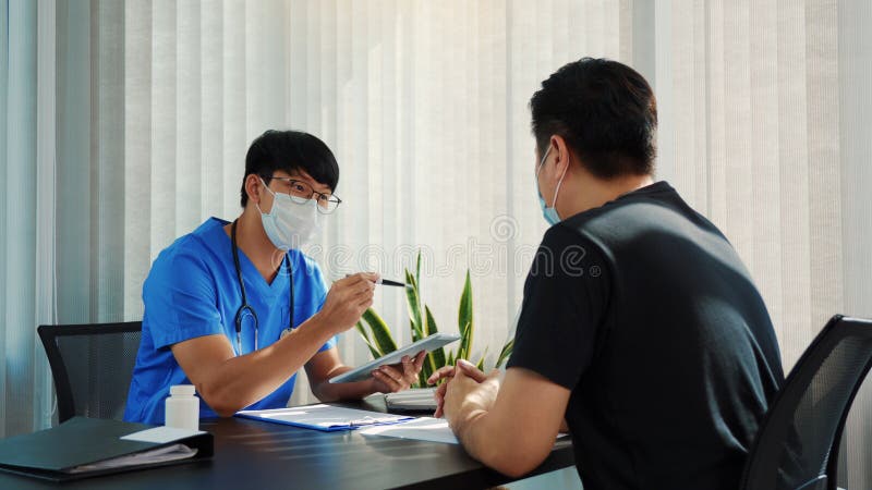 Los médicos están explicando el tratamiento de un paciente enfermo en comprimidos mientras lleva una máscara durante el brote de v imágenes de archivo libres de regalías