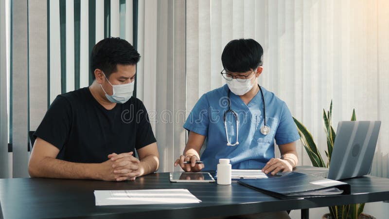 Los médicos están explicando el tratamiento de un paciente enfermo en comprimidos mientras lleva una máscara durante el brote de v fotos de archivo