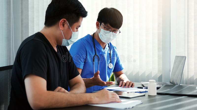 Los médicos están explicando el tratamiento de un paciente enfermo en comprimidos mientras lleva una máscara durante el brote de v fotos de archivo