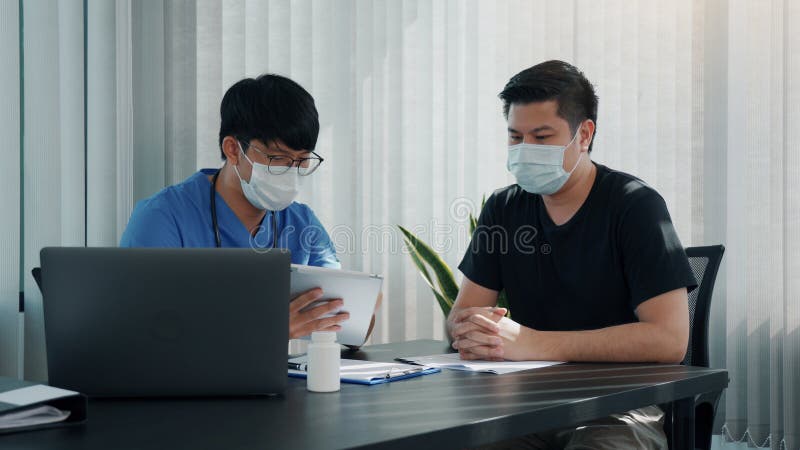 Los médicos están explicando el tratamiento de un paciente enfermo en comprimidos mientras lleva una máscara durante el brote de v fotos de archivo