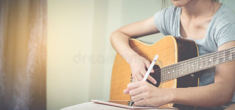 Los músicos de sexo femenino tocan la guitarra y escriben canciones usando la tableta Th foto de archivo libre de regalías Los músicos de sexo femenino tocan la guitarra y escriben canciones usando la tableta Th foto de archivo libre de regalías
