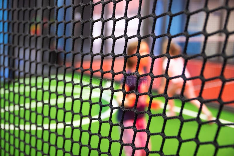 Blurred children are playing behind the net at indoor playground in activity park.