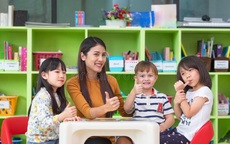 Los niños asiáticos del profesor de sexo femenino y de la raza mixta manosean con los dedos para arriba en sala de clase, fotos de archivo libres de regalías Los niños asiáticos del profesor de sexo femenino y de la raza mixta manosean con los dedos para arriba en sala de clase, fotos de archivo libres de regalías