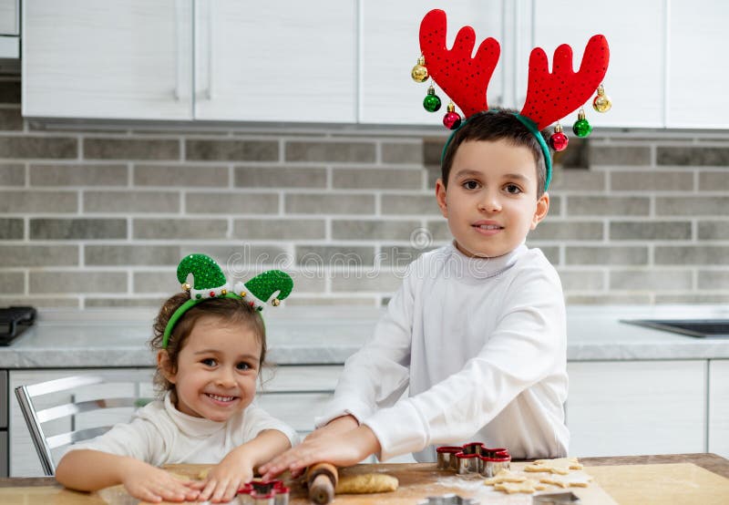 Los niños con decoraciones de Navidad en sus cabezas preparan el pan de jengibre de Navidad de masa. Preparación para la Navidad imagen de archivo libre de regalías