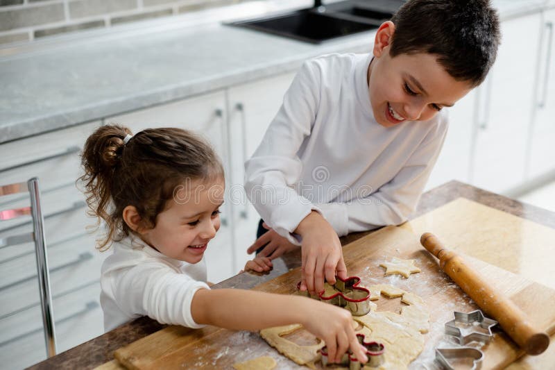 Los niños le cortaron los espacios en blanco para pasteles de masa. El hermano y la hermana se preparan para celebrar la Navidad foto de archivo