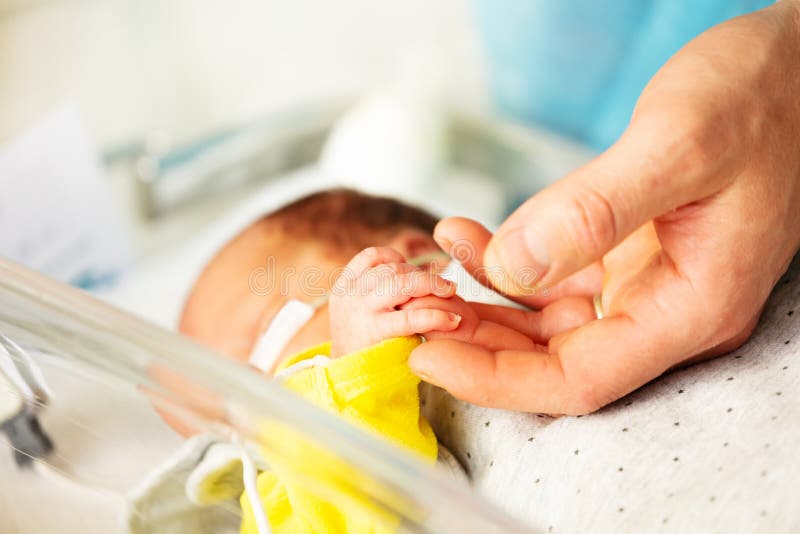 Close up of a father`s hand and premature born infant child in ICU hospital room with monitor on. Close up of a father`s hand and premature born infant child in ICU hospital room with monitor on