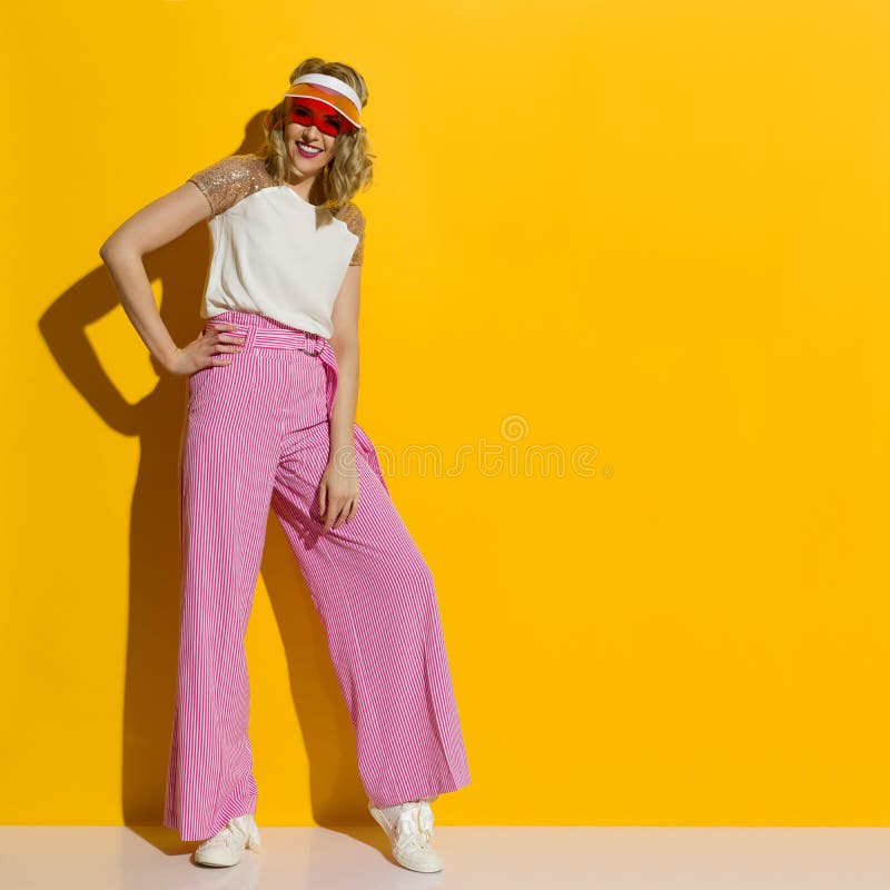 Los pantalones sonrientes de las piernas de In Striped Wide del modelo de moda y la visera transparente se est? colocando en la l foto de archivo Los pantalones sonrientes de las piernas de In Striped Wide del modelo de moda y la visera transparente se est? colocando en la l foto de archivo