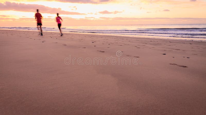 Los pares están corriendo en la playa en la salida del sol imagen de archivo libre de regalías Los pares están corriendo en la playa en la salida del sol imagen de archivo libre de regalías