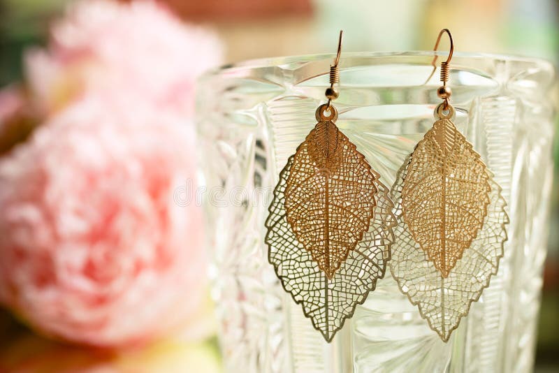 Los pendientes de oro de las señoras se van cerca para arriba en fondo colorido borroso con las flores fotografía de archivo Los pendientes de oro de las señoras se van cerca para arriba en fondo colorido borroso con las flores fotografía de archivo
