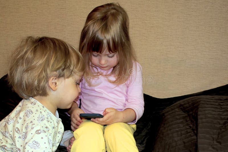 Los pequeños gemelos rubios curiosos lindos miran historietas en smartphone imágenes de archivo libres de regalías Los pequeños gemelos rubios curiosos lindos miran historietas en smartphone imágenes de archivo libres de regalías