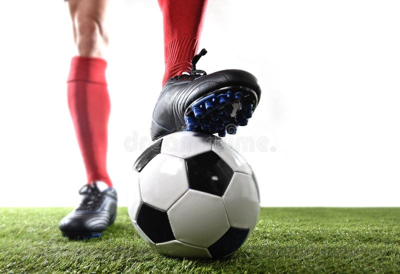 Los pies de las piernas del futbolista en calcetines rojos y zapatos negros que presentan con la bola que juega en hierba verde e foto de archivo libre de regalías Los pies de las piernas del futbolista en calcetines rojos y zapatos negros que presentan con la bola que juega en hierba verde e foto de archivo libre de regalías