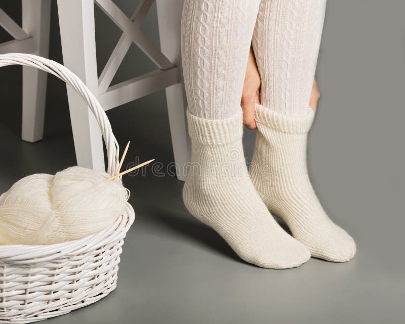 Female feet in white knitted stockings and socks near the basket with yarn and knitting. Female feet in white knitted stockings and socks near the basket with yarn and knitting.