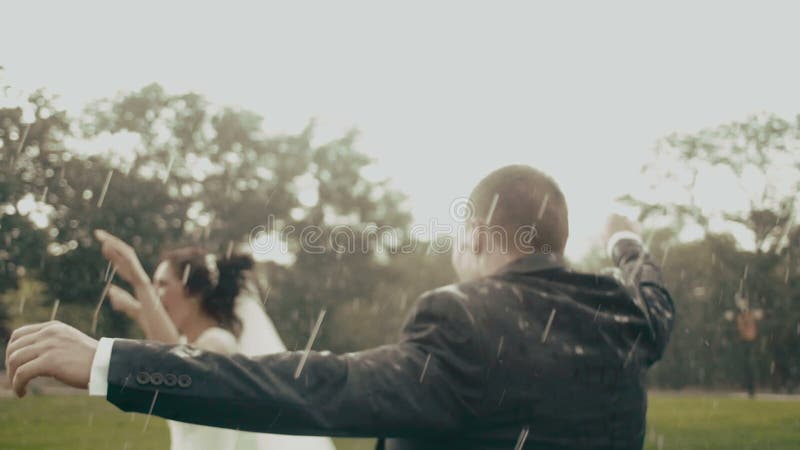 Los recienes casados felices están bailando en la lluvia en el parque durante el verano