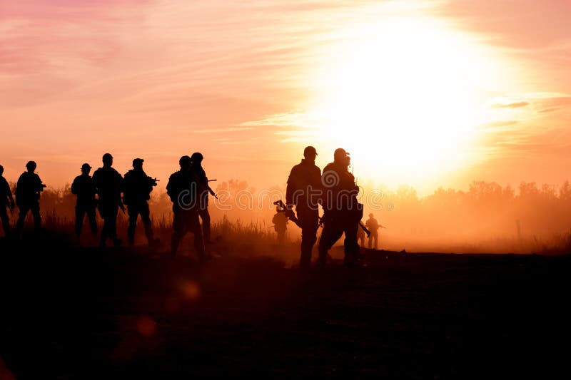 Los soldados de la acción de la silueta que caminan las armas del control el fondo son oscuridad del humo y del puesta del sol y fotografía de archivo libre de regalías Los soldados de la acción de la silueta que caminan las armas del control el fondo son oscuridad del humo y del puesta del sol y fotografía de archivo libre de regalías