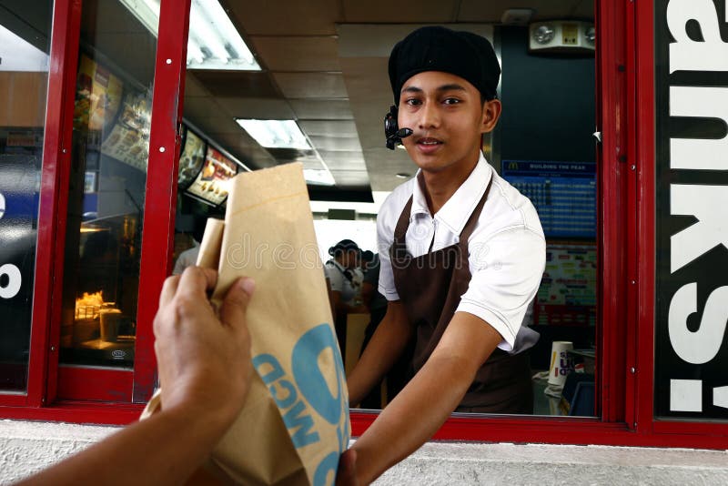 Los trabajadores de un restaurante de comida rápida ofrecen el pedido de comida de un cliente en una unidad a través de la ventan fotografía de archivo libre de regalías