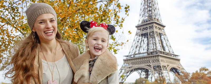 Perfect autumn holidays in Disneyland and Paris. Portrait of smiling tourists mother and daughter in Minnie Mouse Ears on embankment near Eiffel tower in Paris, France sitting on the parapet. Perfect autumn holidays in Disneyland and Paris. Portrait of smiling tourists mother and daughter in Minnie Mouse Ears on embankment near Eiffel tower in Paris, France sitting on the parapet