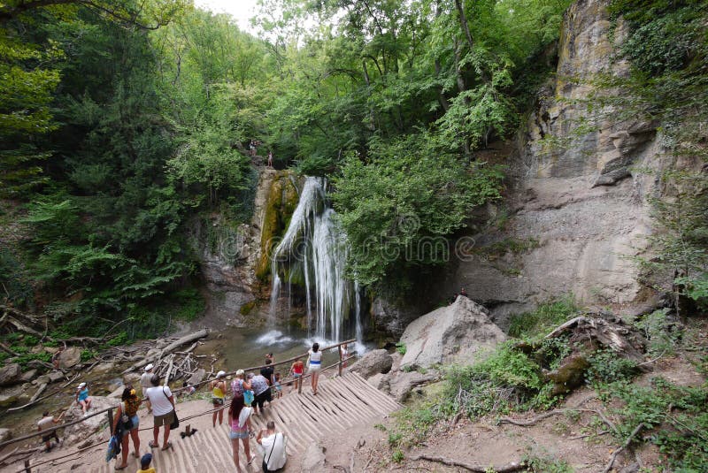 Los turistas miran y fotografían una cascada hermosa de la montaña en una plataforma de la visión cerca de la montaña rocosa fotos de archivo Los turistas miran y fotografían una cascada hermosa de la montaña en una plataforma de la visión cerca de la montaña rocosa fotos de archivo