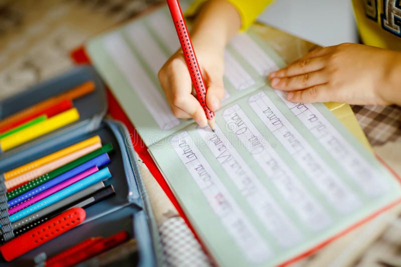 Lose-up of little kid boy at home making homework, child writing first letters and words like mama with colorful pens