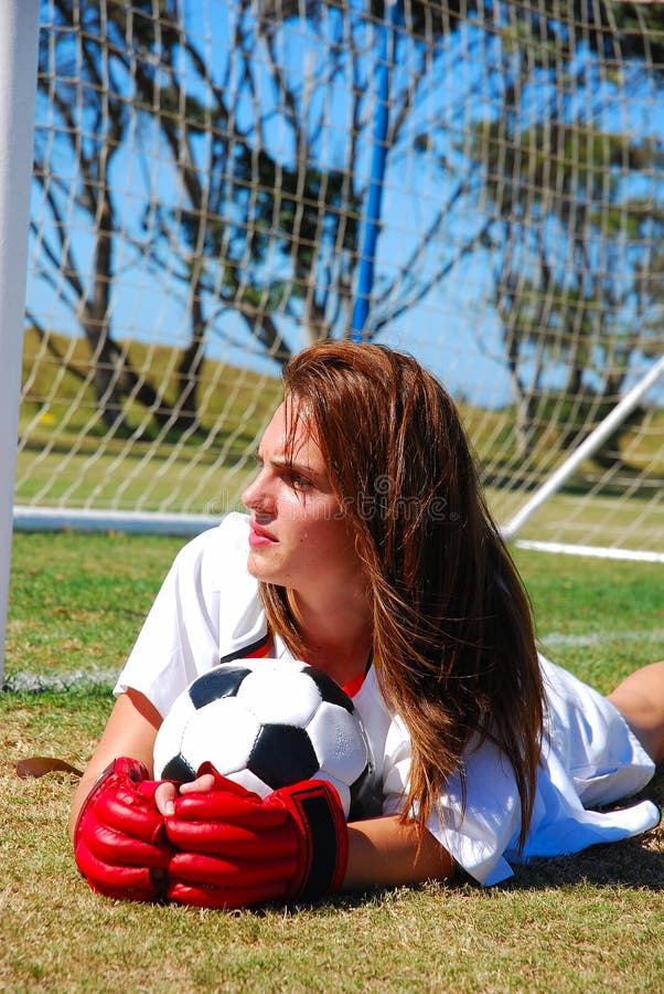 Una bella caucasica bianca adolescenti portiere deluso espressione del viso disteso sul campo con il pallone da calcio fissando dopo aver perso un partita di calcio.