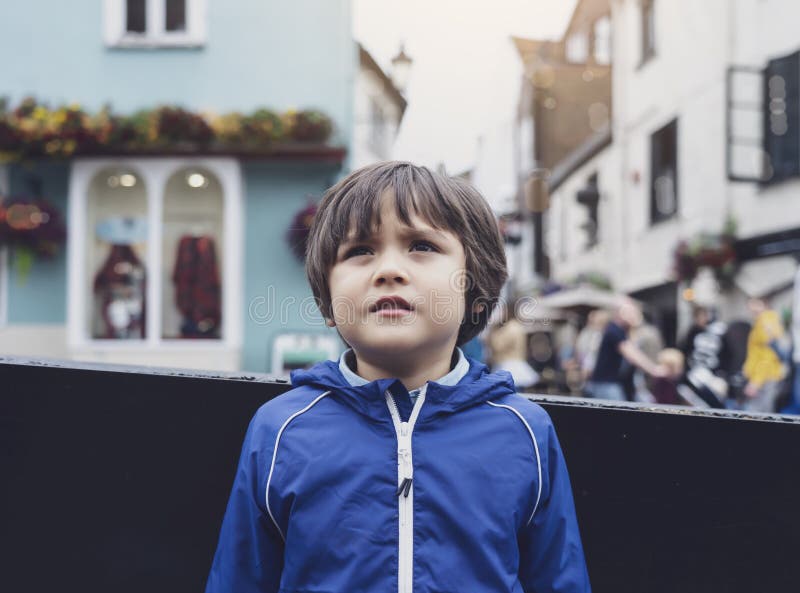 Lost child boy standing on a busy street in a center of city, Kid with worrying face looking around with blurry background of