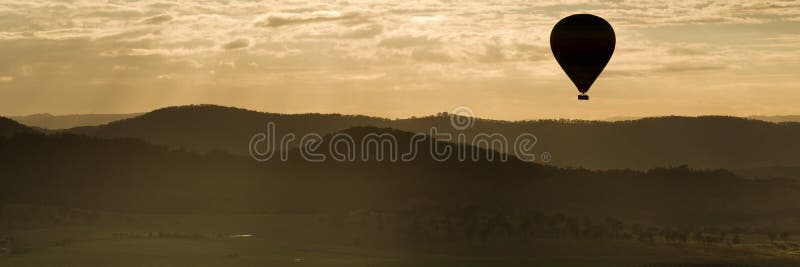 Silhouette panorama of a hot air balloon floating over hilly countryside at sunset. Silhouette panorama of a hot air balloon floating over hilly countryside at sunset.