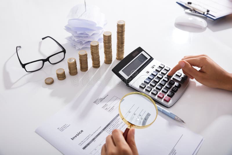 Businessperson`s Hand Analyzing Bills With Magnifying Glass In Front Of Stacked Of Coins Graph. Businessperson`s Hand Analyzing Bills With Magnifying Glass In Front Of Stacked Of Coins Graph