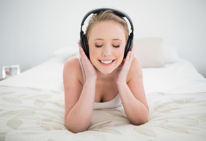 Louro feliz natural que encontra-se na cama e que escuta a música com olhos fechados fotografia de stock royalty free Louro feliz natural que encontra-se na cama e que escuta a música com olhos fechados fotografia de stock royalty free