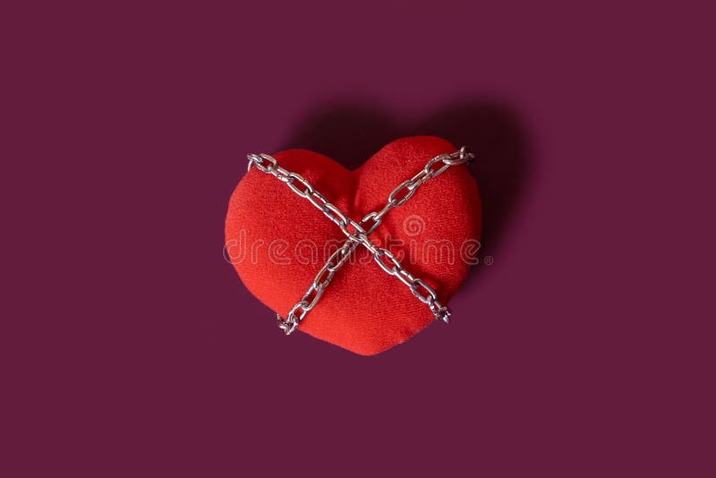 Love addiction. A toy heart rewound by a chain on a colored background