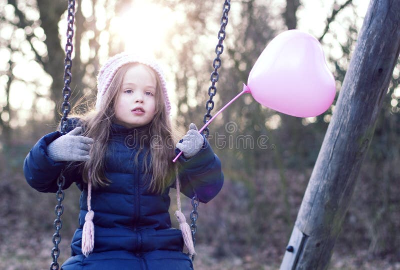 Love concept: child on a swing holding a heart-shaped baloon. stock photos Love concept: child on a swing holding a heart-shaped baloon. stock photos