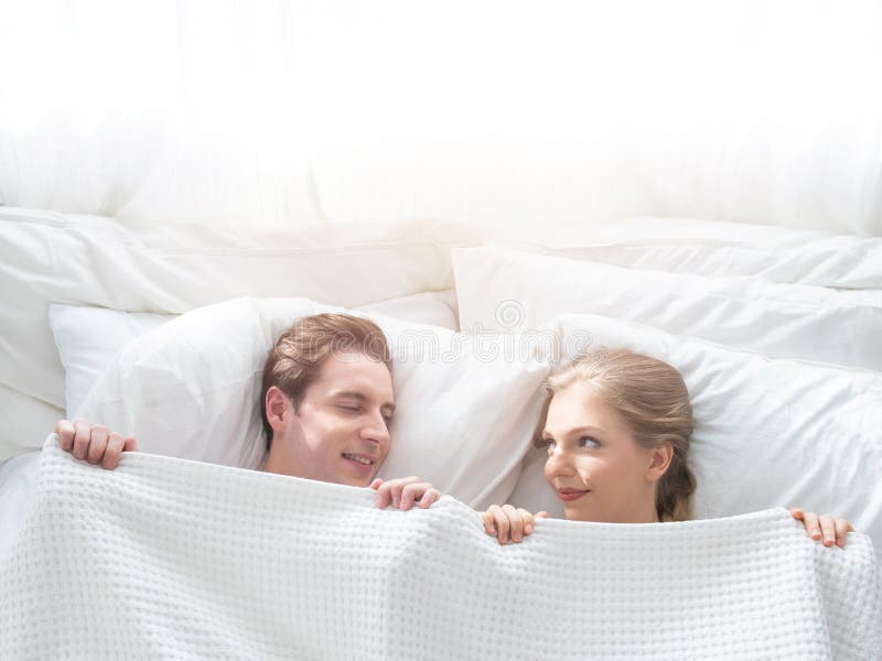 Love and Happiness Concept .Funny Married Couple Lying in Bed and Hiding Under White Blanket, Looking at Camera with Eyes Full of Stock Image picture
