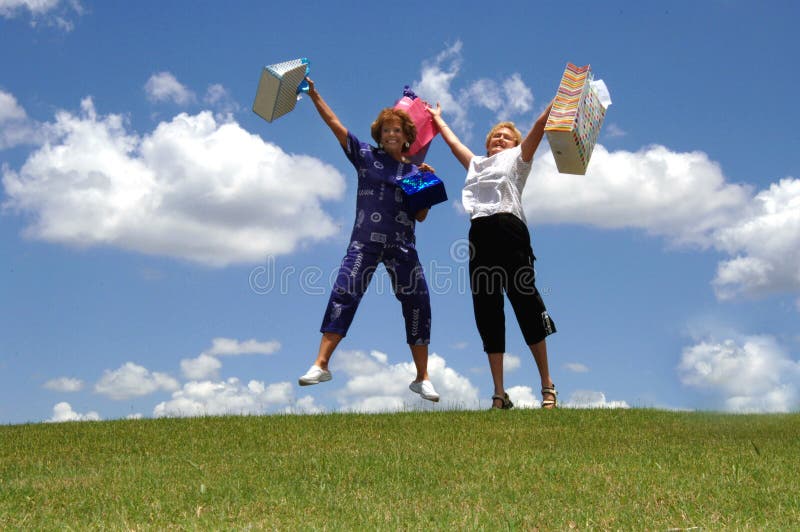 Two happy senior women holding up shopping bags jumping outdoors. Two happy senior women holding up shopping bags jumping outdoors