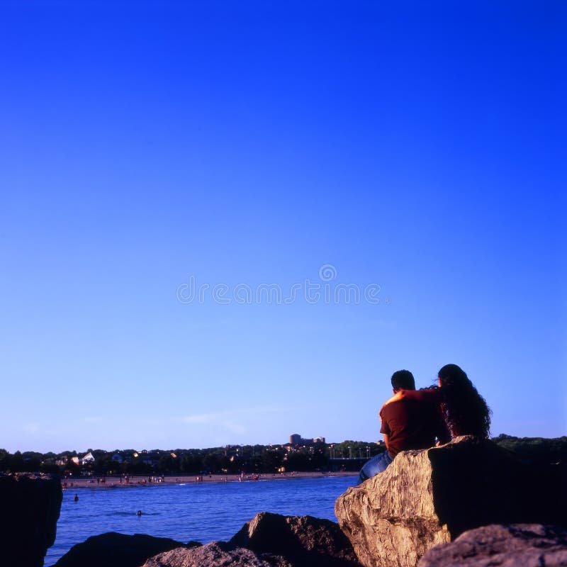 A couple sitting on rocks overlooking a beachfront. Taken with a medium format TLR and Fuji Velvia 100. A couple sitting on rocks overlooking a beachfront. Taken with a medium format TLR and Fuji Velvia 100.