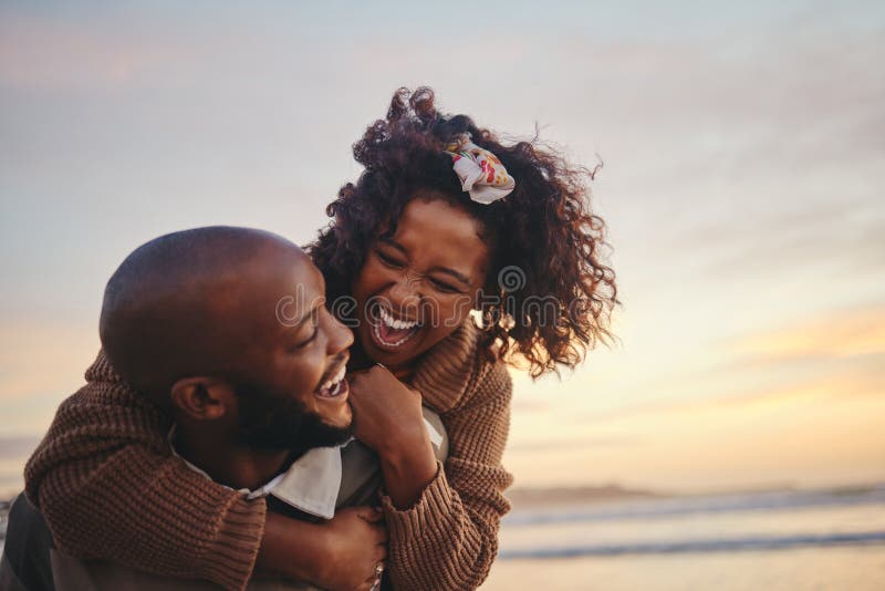 Love, travel and fun couple at beach enjoying summer vacation or honeymoon at sunset with a piggy back ride while being