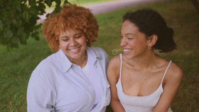 Lovely Beautiful Happy Lesbian African American Couple Sitting On Green Grass Hugging Outside At