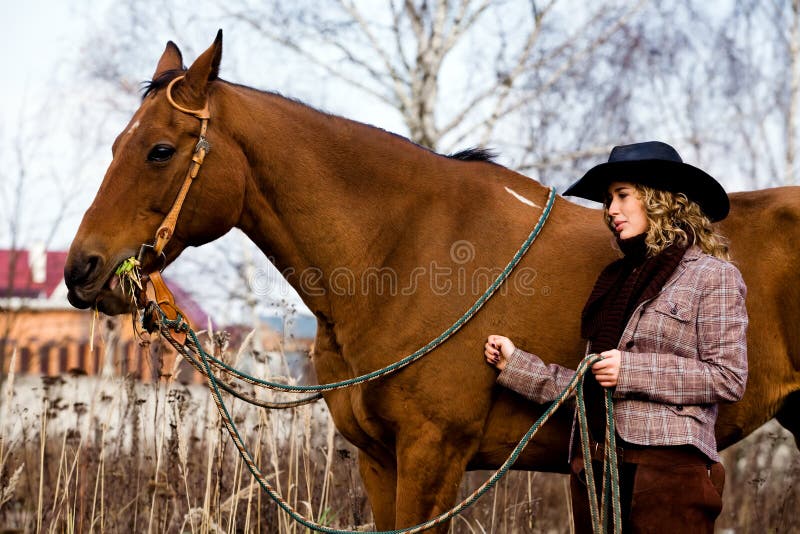 Lovely blond woman in a hat standing by horse