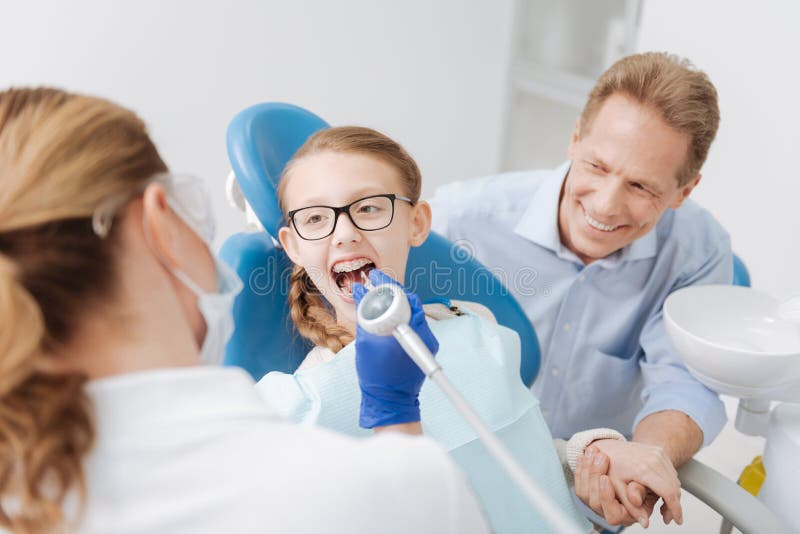 Great parent. Precise wonderful clever dentist conducting a procedure employing professional equipment while the parent sitting beside his girls and supporting her. Great parent. Precise wonderful clever dentist conducting a procedure employing professional equipment while the parent sitting beside his girls and supporting her