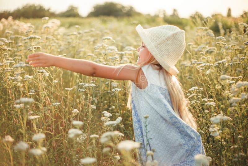Lovely smiling blond girl in a field at sunset. Cute girl in a flowering field sniffs flowers. Ukrainian in a hat and dress near royalty free stock photo Lovely smiling blond girl in a field at sunset. Cute girl in a flowering field sniffs flowers. Ukrainian in a hat and dress near royalty free stock photo