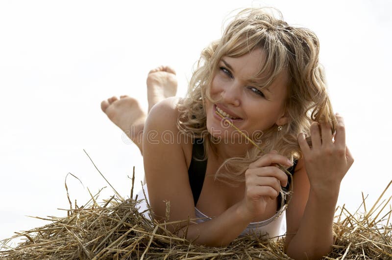 Lovely smiling woman lying on haystack outdoors