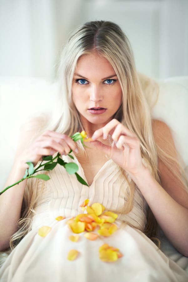 He loves me.... Portrait of an attractive woman pulling petals from a rose on her bed.