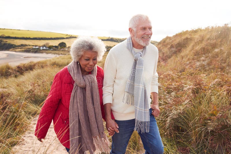 Loving Active Senior Couple Walking Arm In Arm Through Sand Dunes On Winter Beach Vacation royalty free stock image