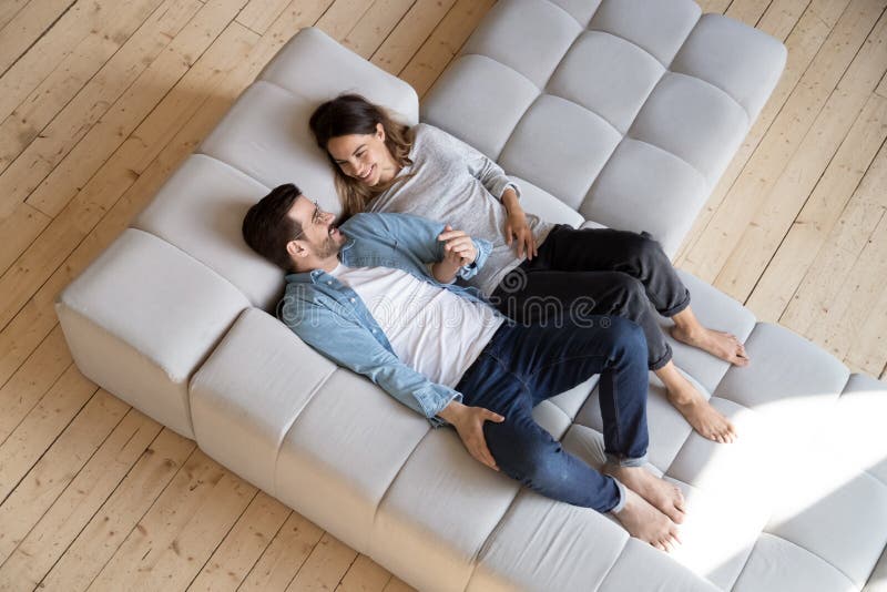 Loving couple holding hands, relaxing on cozy sofa top view