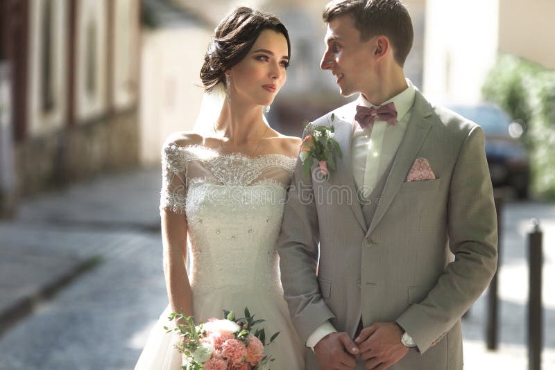 A loving couple of newlyweds walks in the city, and smile. The bride in a beautiful dress, the groom dressed stylishly