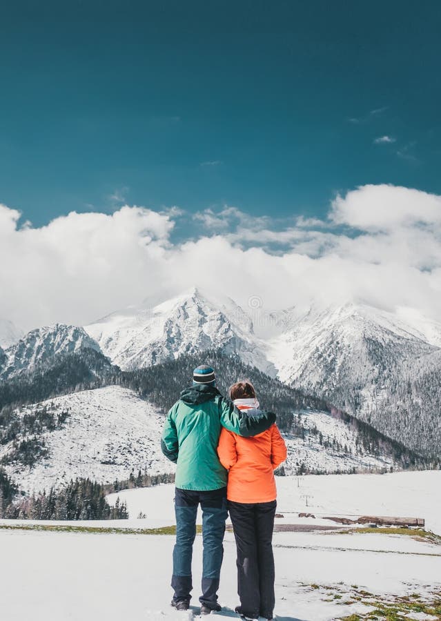 Milující pár stojící a při pohledu na krásné zasněžené vrcholky hor. Vertikální panoramatický pohled. Pohled zezadu
