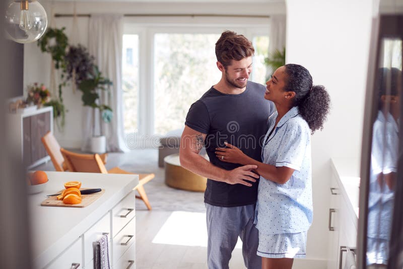 Loving Couple Wearing Pyjamas Hugging In Kitchen At Home Together stock images