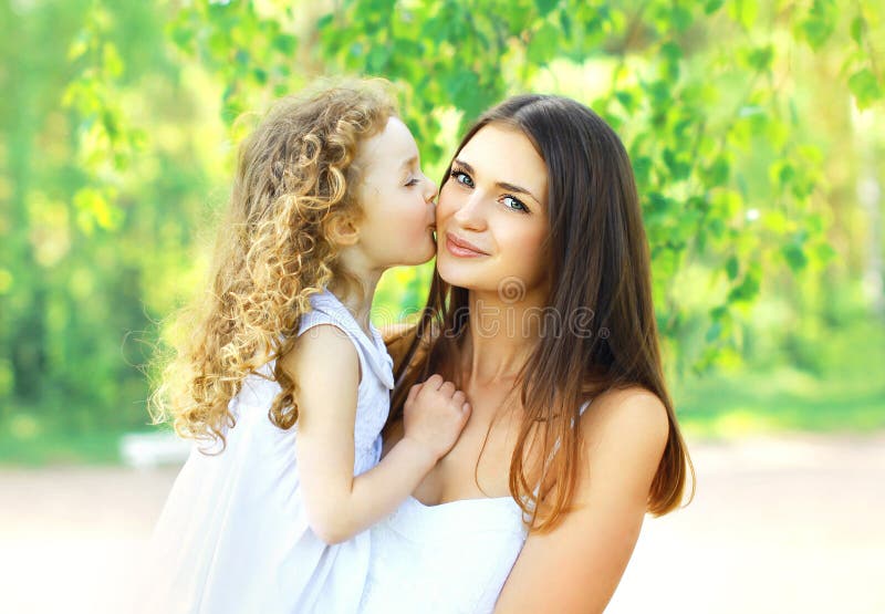 Loving daughter kissing mother, happy young mom and child in warm sunny summer day on the nature