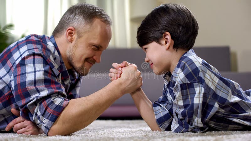 Loving father and kid arm wrestling on the floor, weekend leisure at home, fun royalty free stock photography Loving father and kid arm wrestling on the floor, weekend leisure at home, fun royalty free stock photography